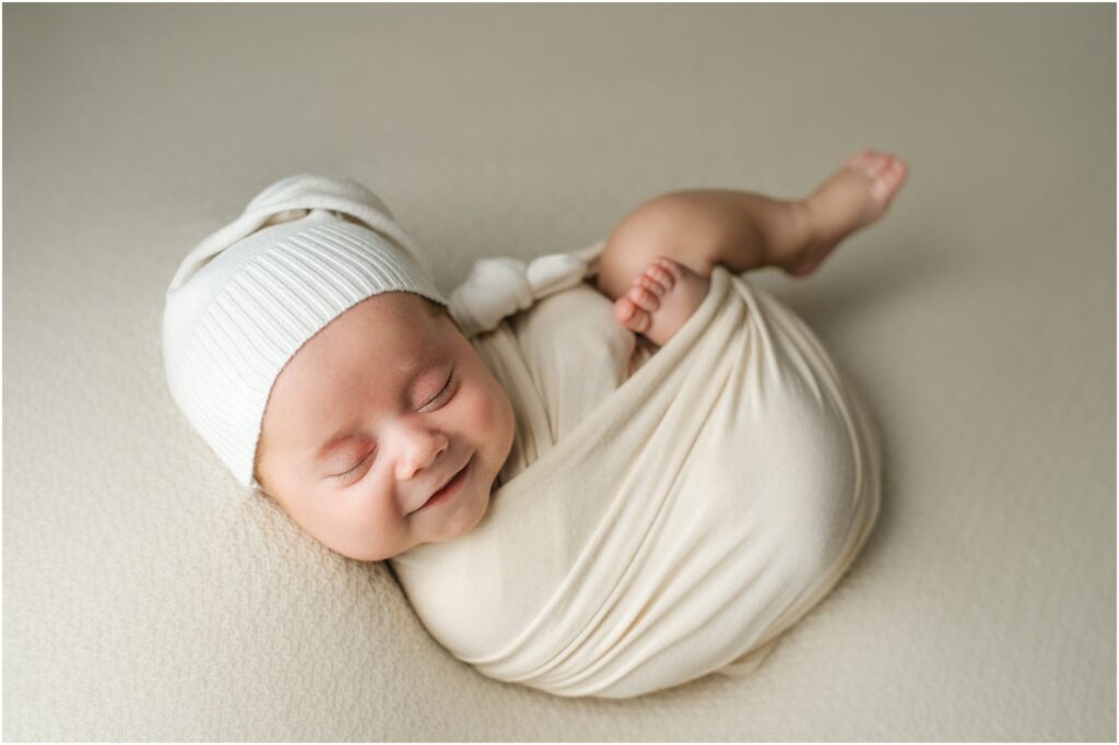 maximus newborn session, smiling baby boy on cream backdrop with cream wrap and hat