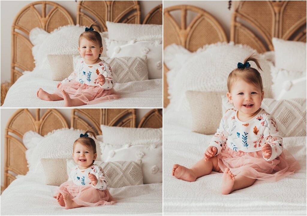 1 year old in pink dress with blue and orange flowers smiling on bed